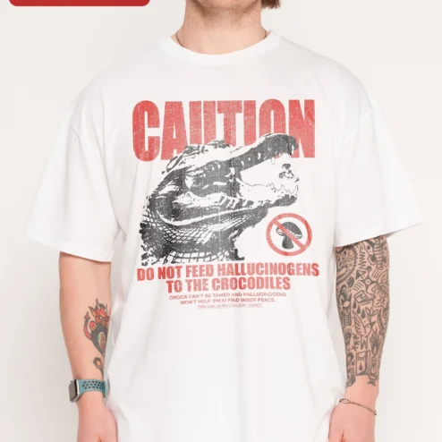 Caution Do Not Feed Hallucinogens To The Crocodiles Funny Graphic Tee on a hanger, ready to ship from Chicago, Illinois