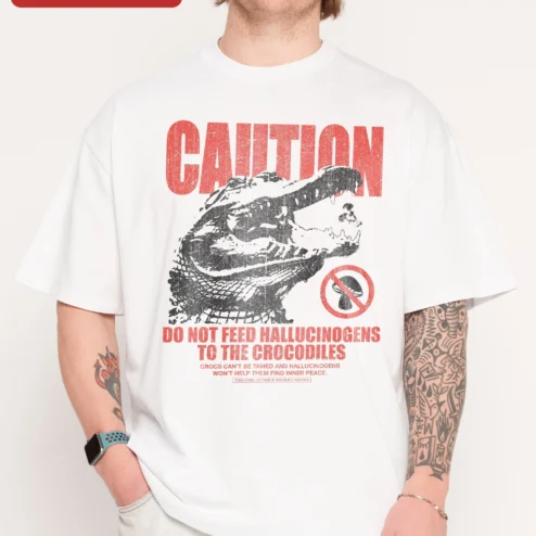 Caution Do Not Feed Hallucinogens To The Crocodiles Funny Graphic Tee Vintage Distressed Shirt on a hanger, ready to ship from Chicago, Illinois